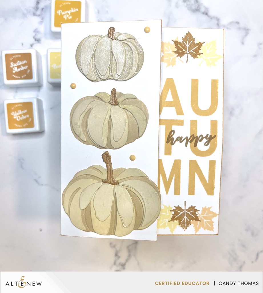 A greeting card featuring three stylized pumpkins in soft colors, with the word 'AUTUMN' prominently displayed alongside decorative leaves.